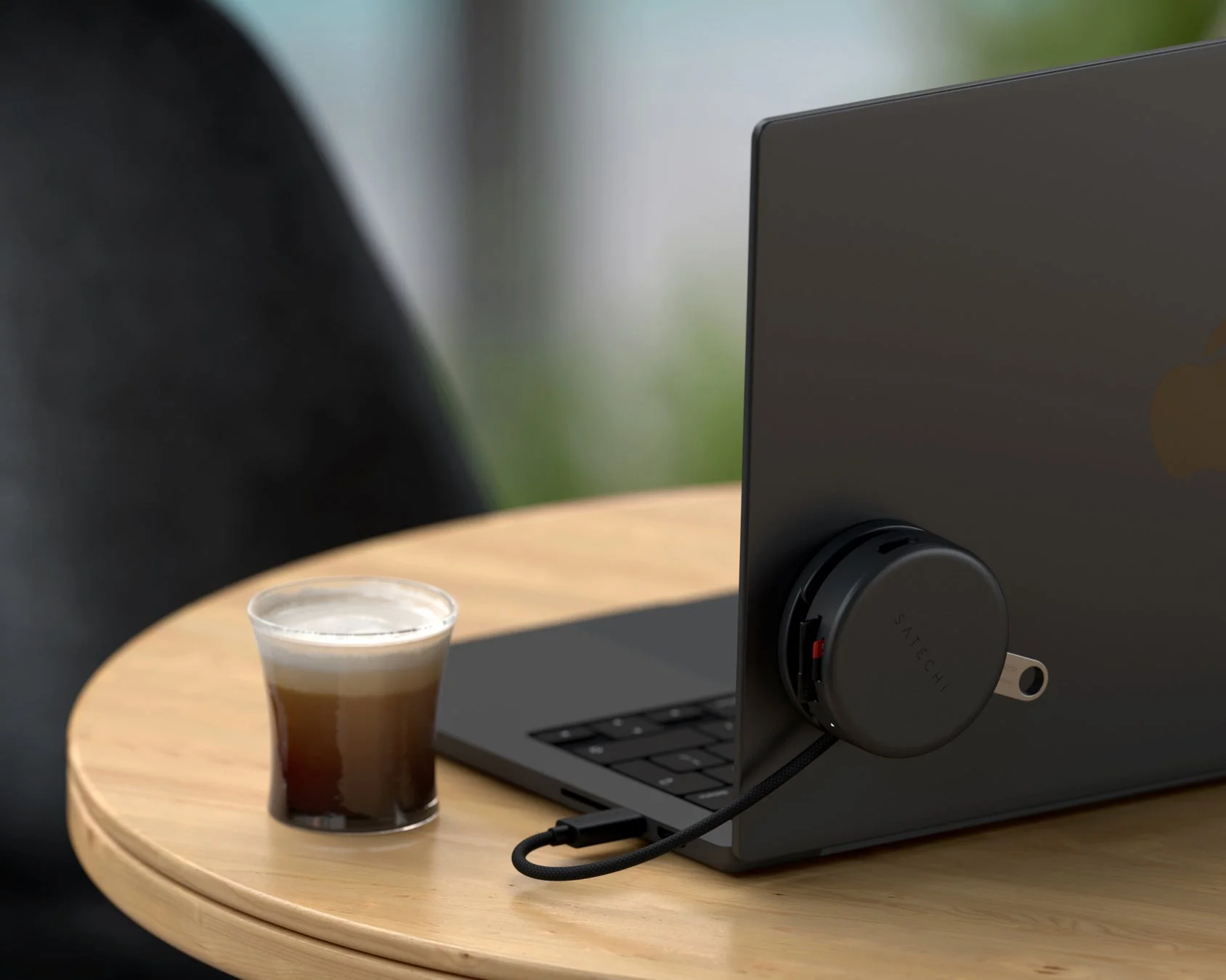 木製のテーブルに置かれた黒いラップトップの側面にSatechi製の丸いUSBハブが接続されている