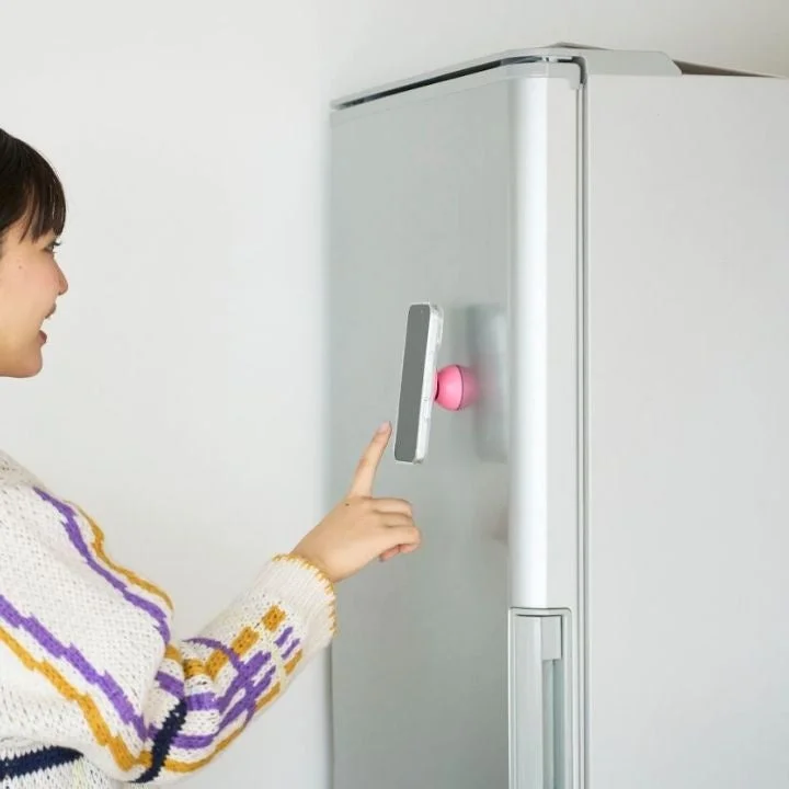 女性が冷蔵庫の側面にマグネットで取り付けられたスマートフォンを指で操作しています。