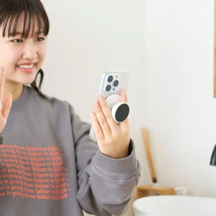 笑顔の若い女性が、スマホグリップを取り付けたスマートフォンを手に持っています。